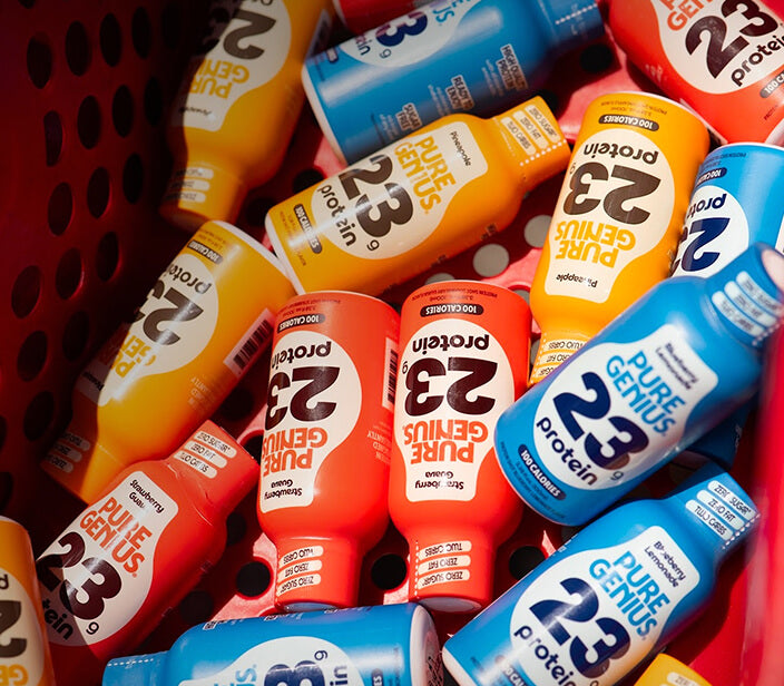 A fridge shelf stocked with a row of Pure Genius protein shots