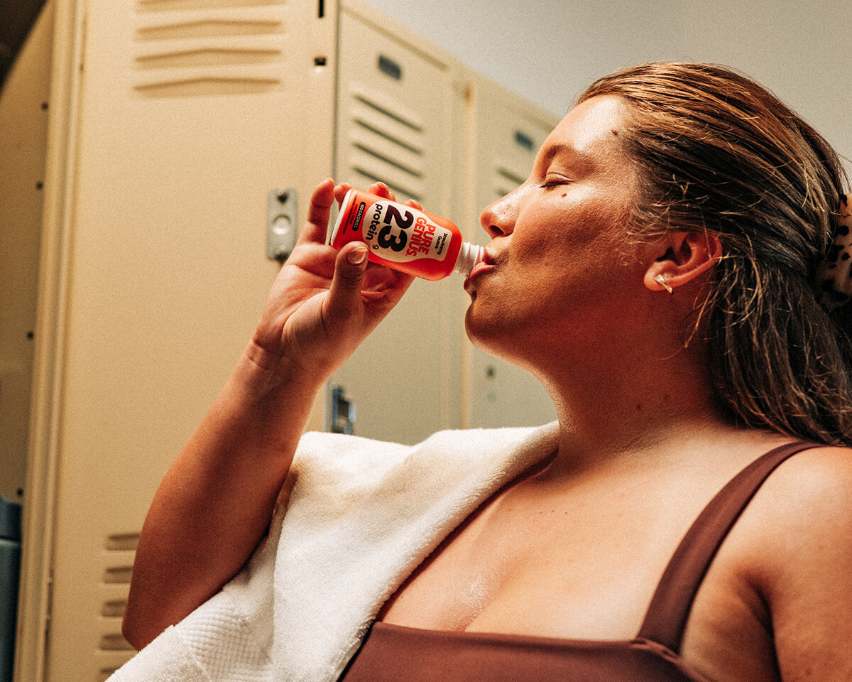 Woman drinking a Pure Genius protein shot in a locker room