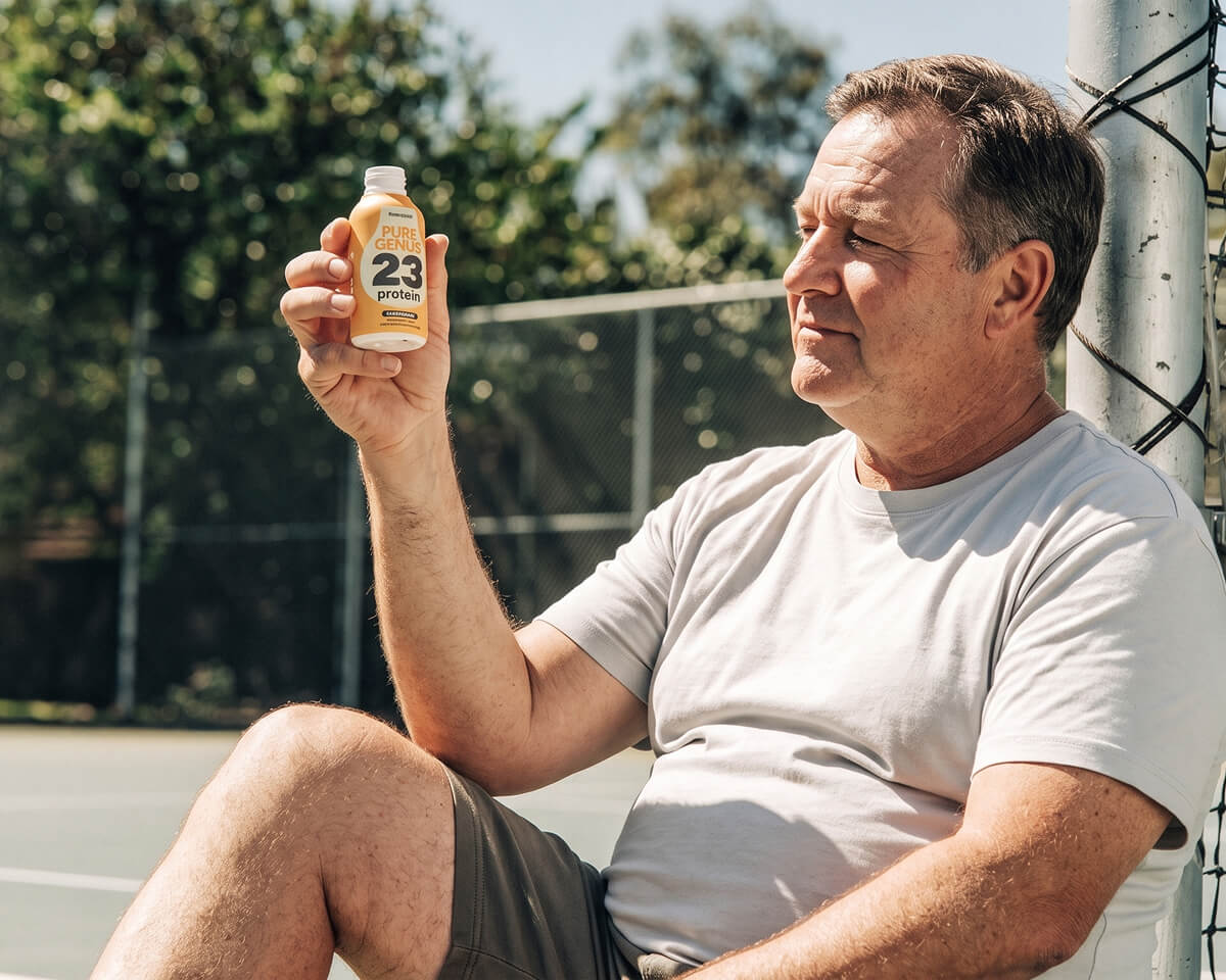 Man holding a Pure Genius protein shot on a tennis court