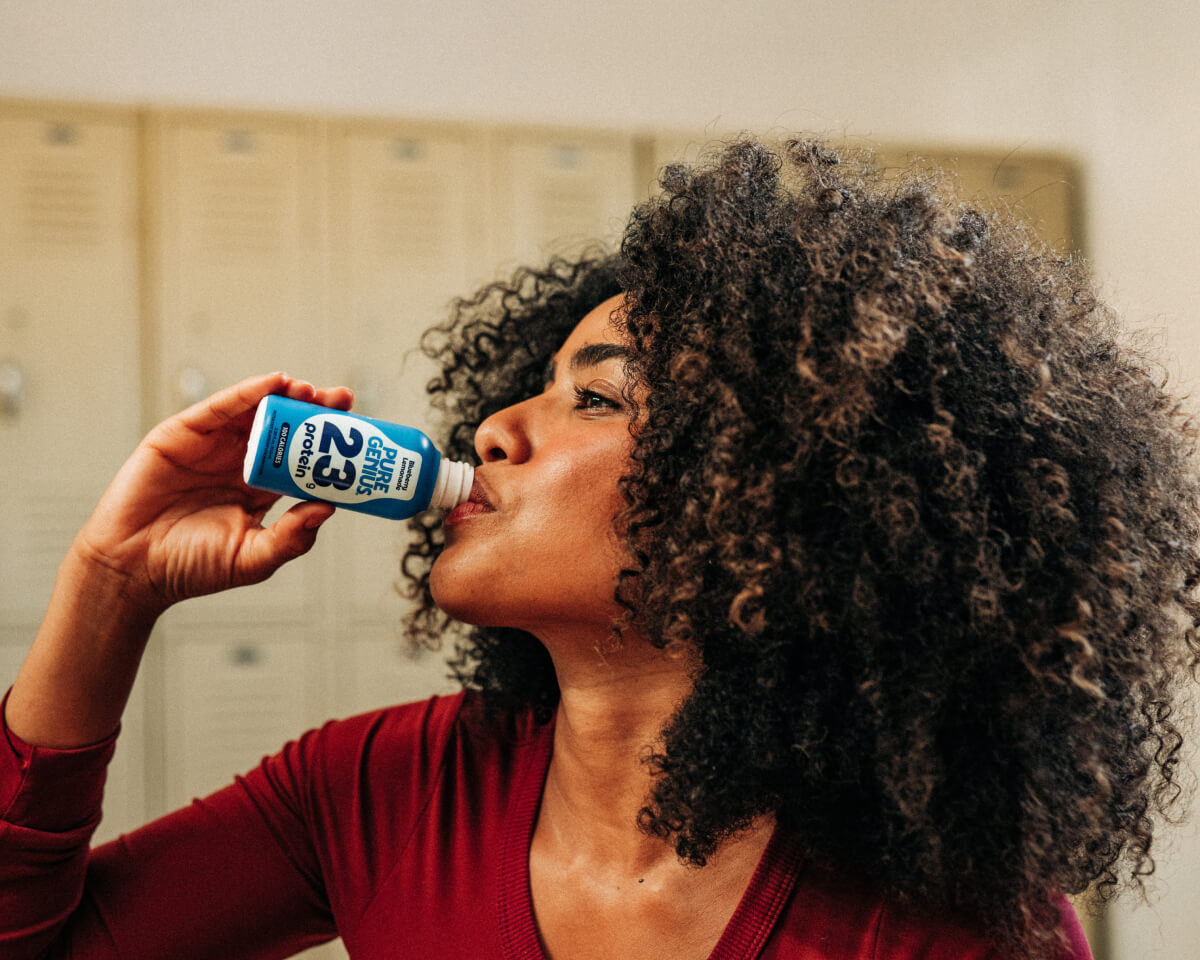 Woman drinking a Pure Genius protein shot in a locker room
