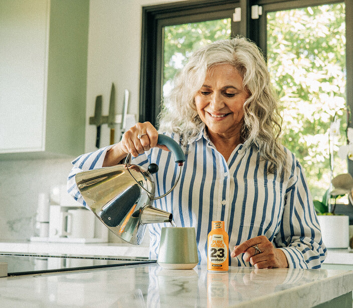 Woman pouring coffee in her kitchen beside a Pure Genius protein shot